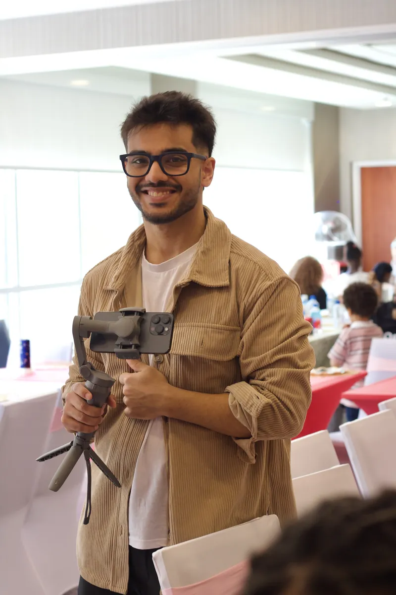 Smiling photographer in glasses and a tan corduroy shirt holding a phone on a gimbal at an event