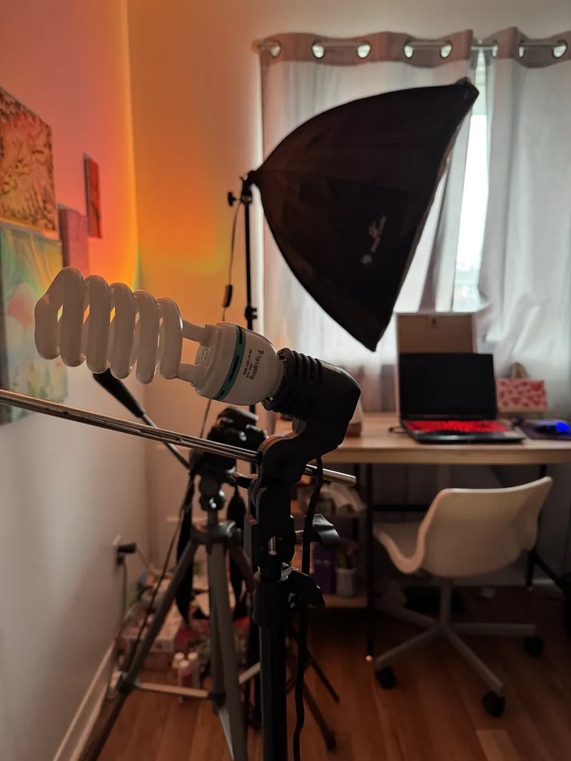 Home photo studio with a softbox, a boom-mounted light, a tripod and a desk with a laptop